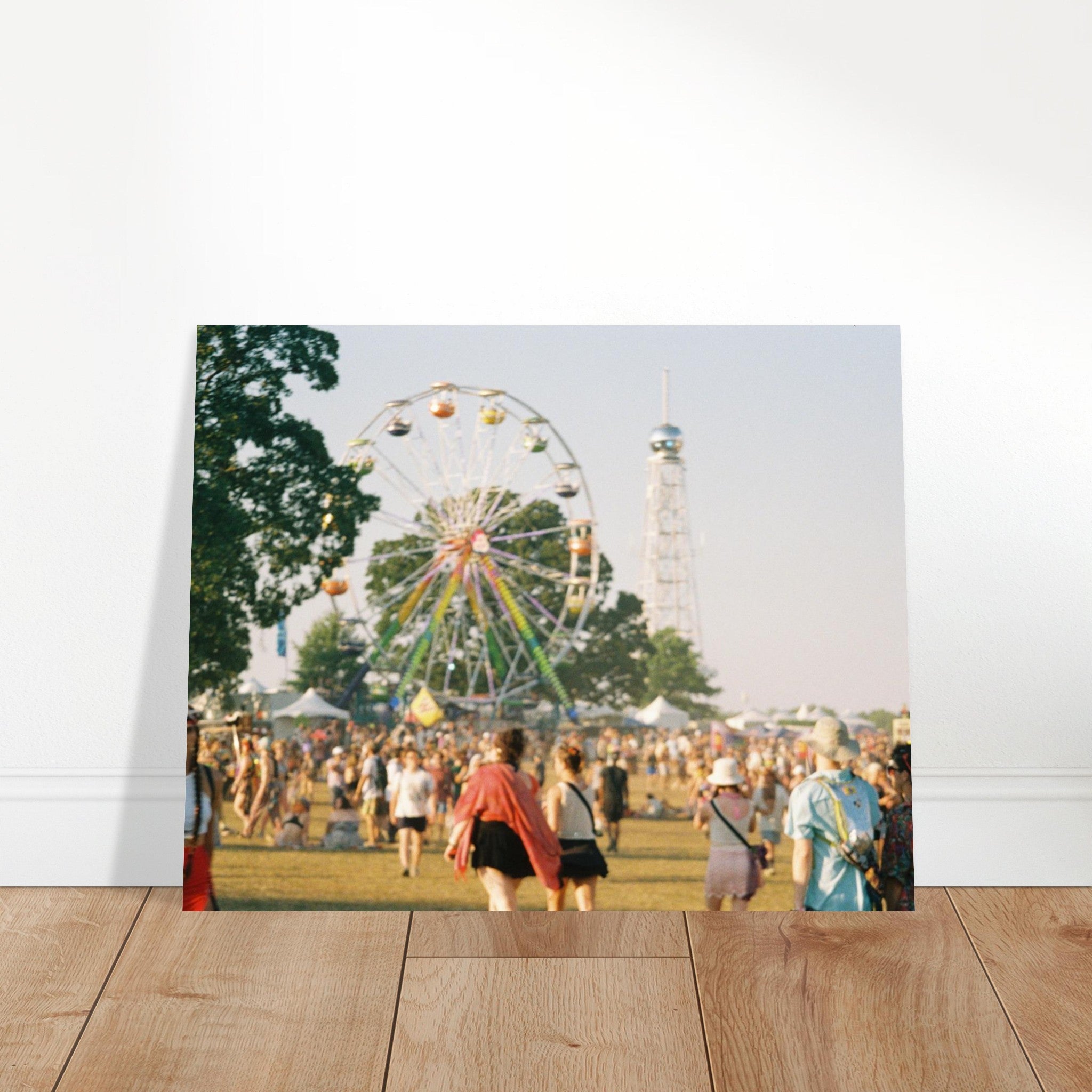 Ferris wheel and tower at a fairground with people around on a wooden floor.