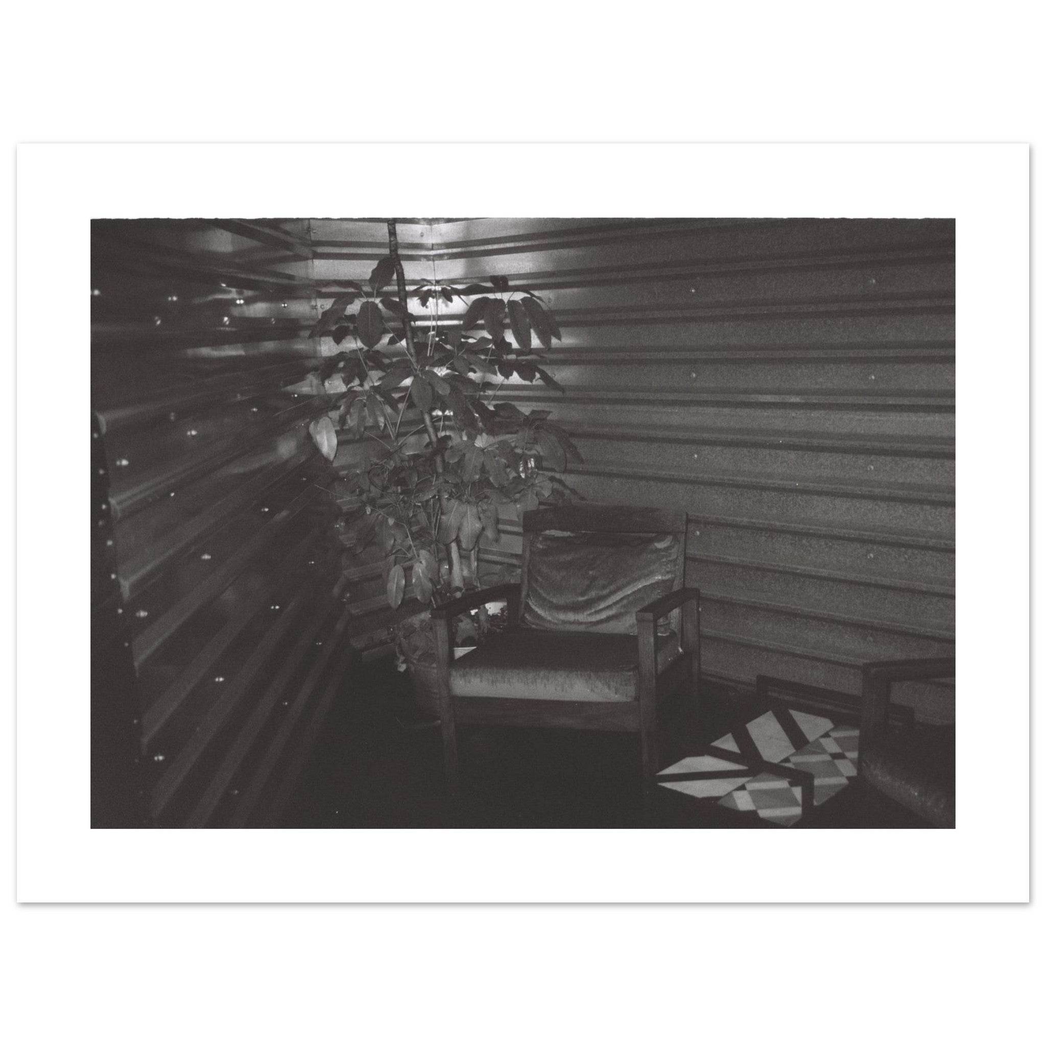 Moody black and white film photo of an empty chair inside a dimly lit room in Mexico City.